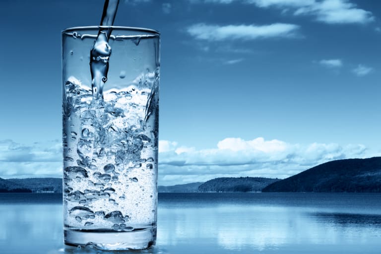pouring pure water into glass with blue landscape background
